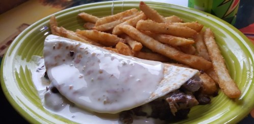 A plate with a quesadilla topped with creamy sauce and a side of golden, crispy French fries.