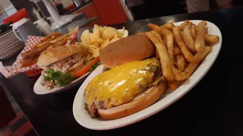 A plate featuring a cheeseburger with fries and chips, alongside a sandwich and more fries in a diner setting.