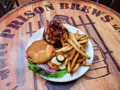 A plate with a burger topped with onion rings, fries, and a side of lettuce, tomato, and pickles on a wooden table.