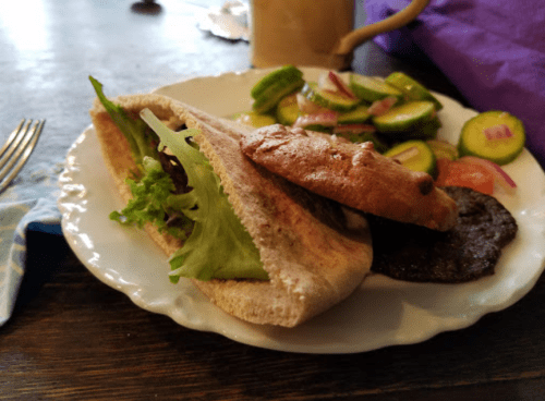 A plate with a pita sandwich filled with lettuce and a side of cucumber salad with tomatoes and onions.