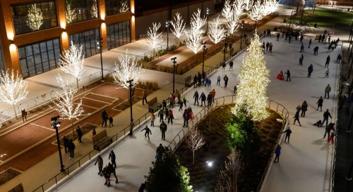 Aerial view of an ice skating rink surrounded by lit trees, with people skating and enjoying the festive atmosphere.