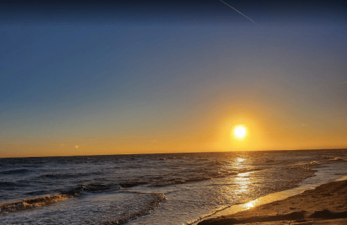 A serene beach at sunset, with golden hues reflecting on the water and gentle waves lapping at the shore.
