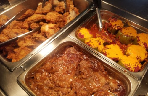 A buffet tray featuring fried chicken, stuffed peppers with cheese, and a savory meat dish in sauce.