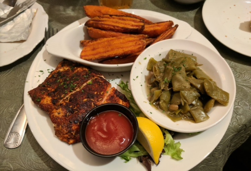 A plate featuring grilled fish, sweet potato fries, green beans, a lemon wedge, and a small cup of ketchup.