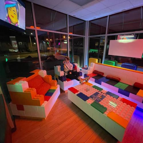 A colorful lounge area made of large building blocks, with a person sitting on a block sofa, illuminated by soft lights.