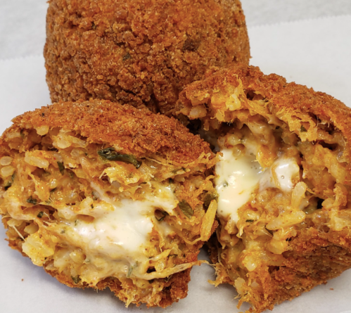 Close-up of crispy fried rice balls, revealing a creamy filling and herbs inside.