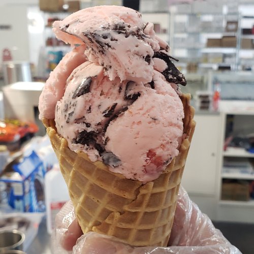 A hand holding a waffle cone filled with pink ice cream mixed with chocolate cookie pieces.