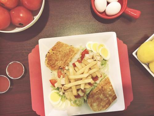 A plate with a salad topped with chicken, fries, and sliced eggs, surrounded by tomatoes and lemons.