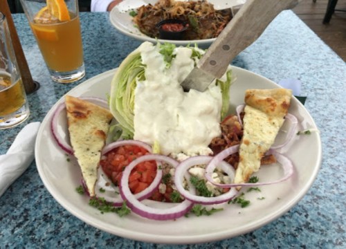 A plate with a wedge of lettuce topped with dressing, tomatoes, onions, and pita bread, alongside a drink.