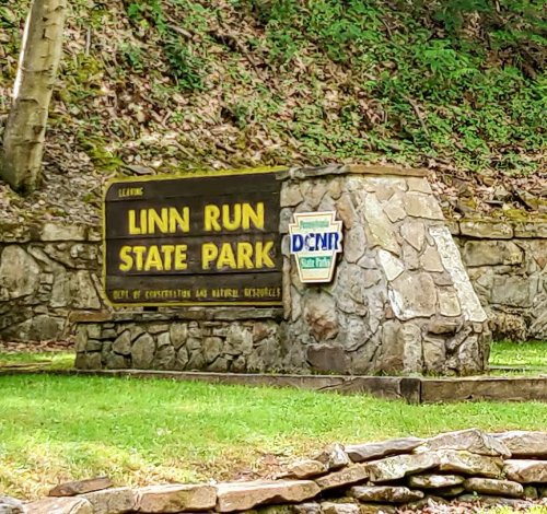 Sign for Linn Run State Park, featuring stone structure and green surroundings, indicating park entrance.
