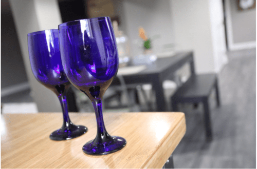 Two elegant purple wine glasses on a wooden surface, with a blurred dining area in the background.