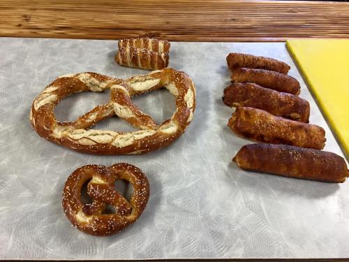 A variety of baked pretzels, including a large pretzel, smaller pretzel knots, and several pretzel sticks on a table.