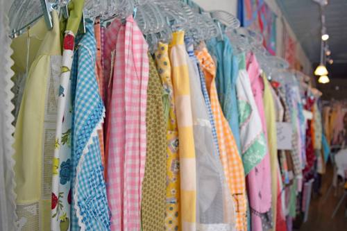 A colorful display of vintage aprons hanging on clear hangers in a shop.