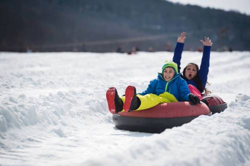 Two children joyfully tubing down a snowy slope, with one raising their hands in excitement.
