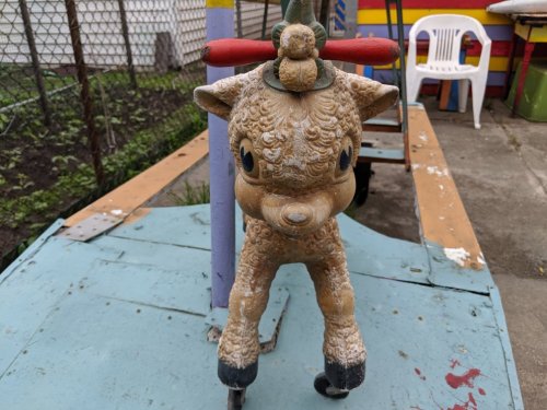 A vintage, weathered toy resembling a sheep on wheels, with a colorful playground background.