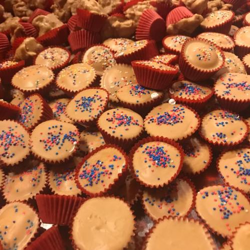 A colorful assortment of small, round candies topped with sprinkles, surrounded by various treats in red cups.