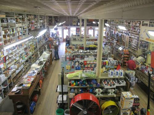 A wide view of a bustling hardware store filled with shelves of tools, supplies, and customers browsing.