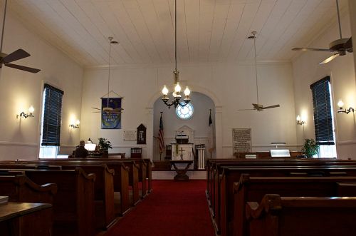 Interior of a church featuring wooden pews, a pulpit, and a large circular window, with soft lighting and a red carpet.