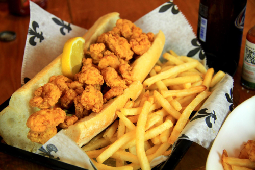 A basket of fried shrimp po'boys with a lemon wedge, served alongside crispy French fries.