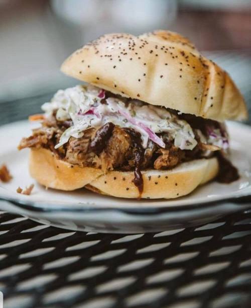 A pulled pork sandwich topped with coleslaw on a poppy seed bun, served on a plate.