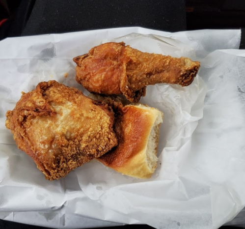 Two pieces of fried chicken and a soft bread roll on white paper.