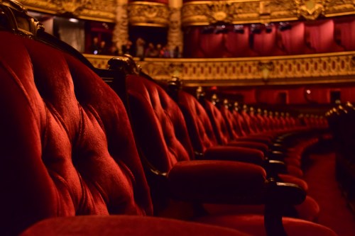 Luxurious red velvet theater seats arranged in a row, with ornate decor in the background.