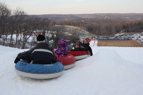 A group of people sitting in snow tubes, preparing to slide down a snowy hill with a scenic view in the background.