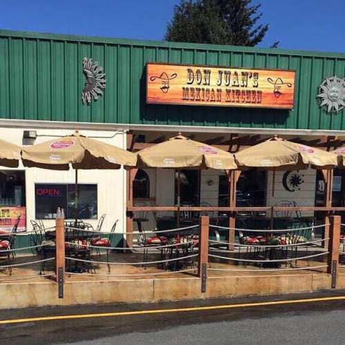 Exterior of Don Juan's Mexican Kitchen, featuring outdoor seating with umbrellas and a vibrant green building.