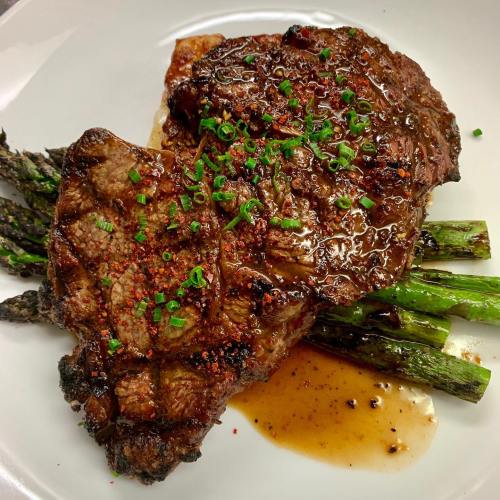 A juicy steak topped with green onions, served on a plate with grilled asparagus and a savory sauce.