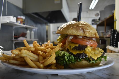 A juicy cheeseburger with lettuce, tomato, and onion, served with a side of crispy fries on a white plate.