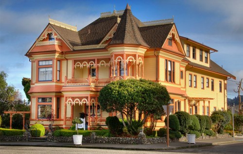 A colorful Victorian-style house with intricate details, surrounded by well-maintained gardens and shrubs.