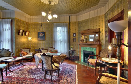 A vintage living room with ornate wallpaper, a patterned rug, elegant furniture, and a fireplace.