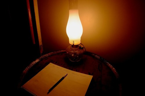 A glowing oil lamp beside a blank notepad and pen on a wooden table, creating a warm, inviting atmosphere.