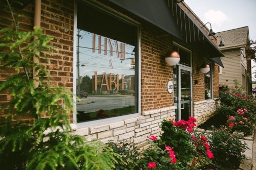 Exterior view of a restaurant with a brick facade, large window displaying "Farm to Table," and colorful flowers in front.