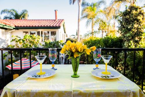A vibrant outdoor table setting with yellow flowers, colorful glasses, and a sunny backdrop of palm trees and greenery.