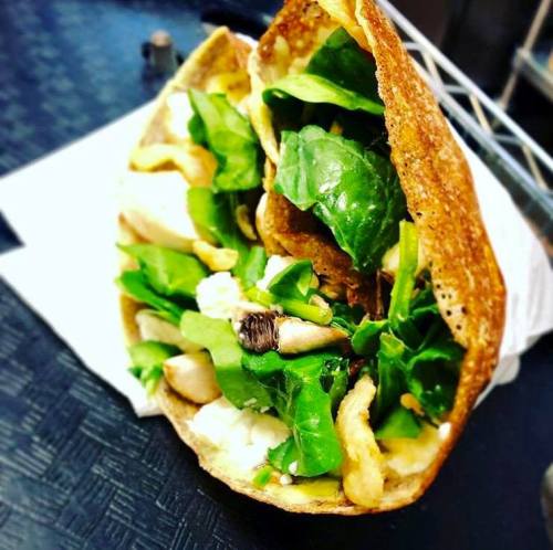 A close-up of a wrap filled with greens, chicken, and other ingredients, resting on a white napkin.