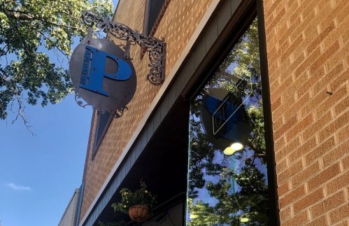 Sign with a blue "P" on a brick building, reflecting trees in the window.