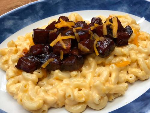 A plate of creamy macaroni and cheese topped with diced, caramelized sausage and shredded cheese.