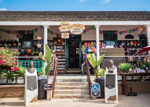 Colorful storefront with decorative items, plants, and plaques, featuring a welcoming entrance and vibrant banners.