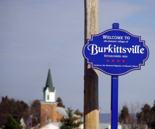Welcome sign for Burkittsville, established 1824, with a church steeple visible in the background.