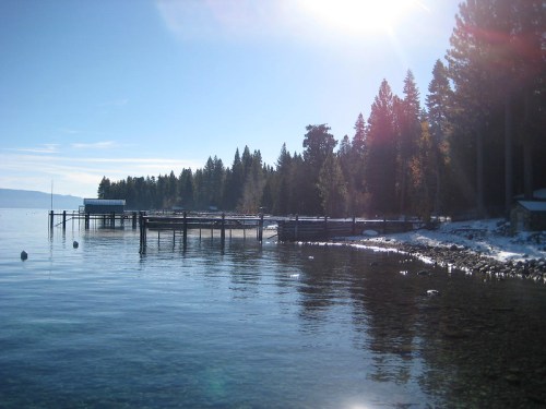 A serene lake scene with a wooden pier, surrounded by tall trees and sunlight reflecting on the water's surface.