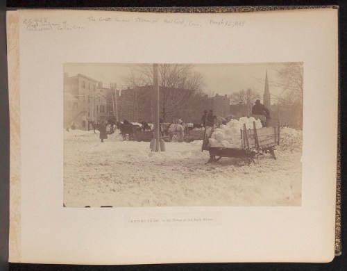 A historic black-and-white photo of horse-drawn sleds transporting snow in a snowy park scene.