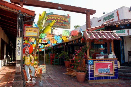 Colorful street scene with vibrant decorations, shops, and a statue of a man in traditional attire.