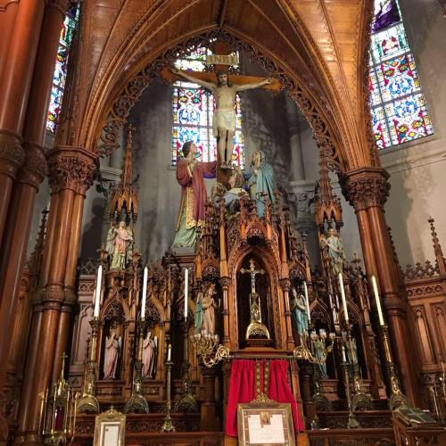 Intricate altar with a crucifix, statues, and stained glass windows in a historic church setting.