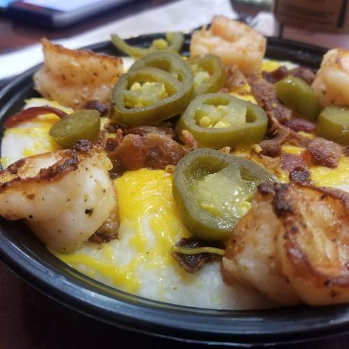 A bowl of creamy grits topped with shrimp, bacon, jalapeños, and melted cheese.