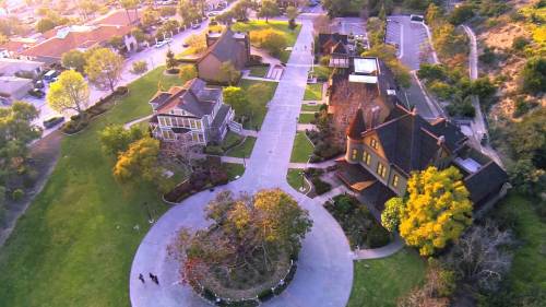 Aerial view of a park with historic buildings, pathways, and trees, surrounded by greenery and a residential area.