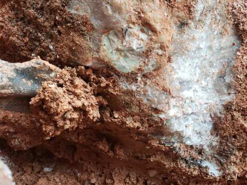 Close-up of rocky soil with a mix of clay and quartz crystals, showcasing earthy textures and mineral formations.