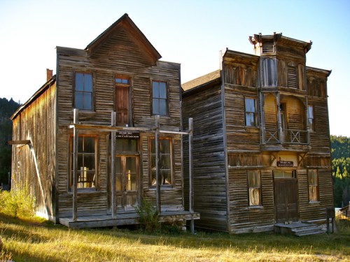 Two old wooden buildings in a ghost town, showcasing rustic architecture against a clear blue sky.