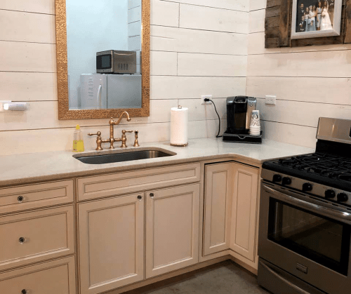 A modern kitchen with a stainless steel stove, sink, and coffee maker, featuring light wood paneling and a decorative mirror.