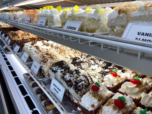 A display of various cakes and desserts, including lemon, vanilla almond, and Oreo whip, in a bakery case.